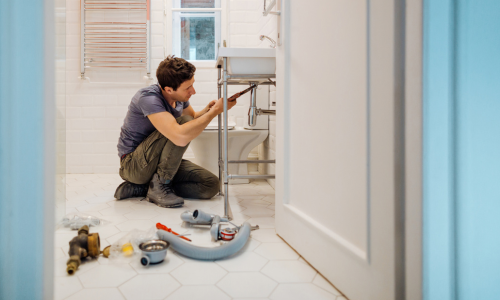 A plumber working underneath a sink surrounded by supplies